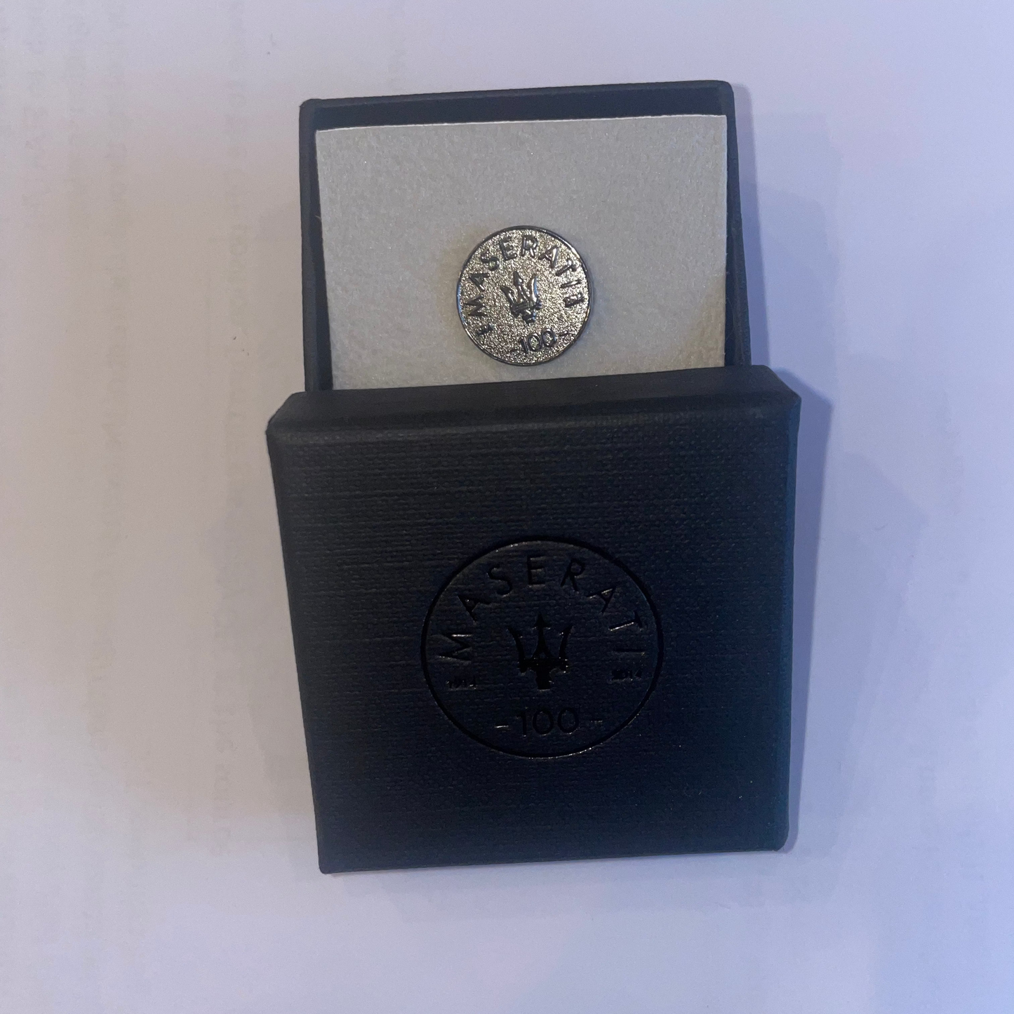 Silver coin in a black display case with Maserati logo on a white background