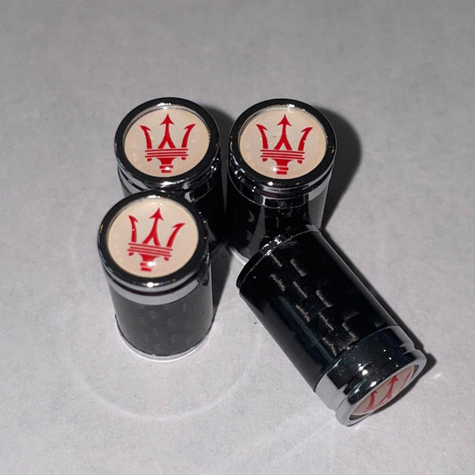 Four black cylindrical wheel caps with red trident logos on the center caps, arranged on a light gray surface.
