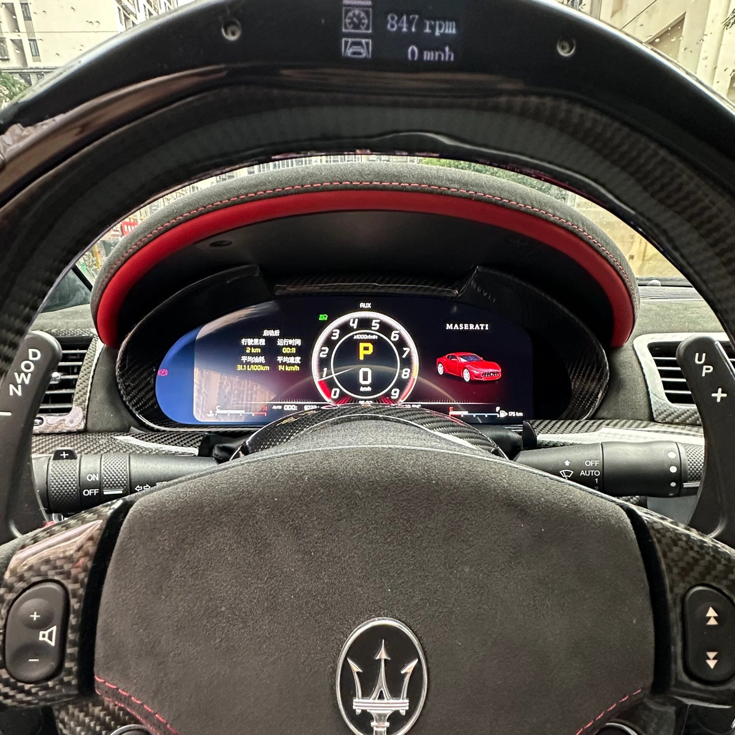 Car interior with steering wheel and dashboard display, showing a Maserati logo.