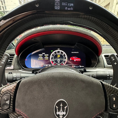 Car interior with steering wheel and dashboard display, showing a Maserati logo.