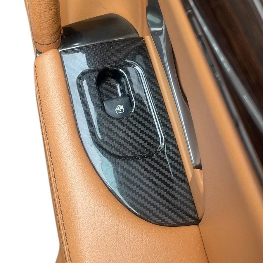 Carbon fiber door panel insert on a car door with tan leather interior.